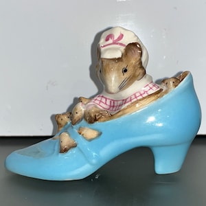 May include: A blue ceramic shoe with a mouse wearing a pink and white dress and hat sitting inside.  There are three smaller mice peeking out of the shoe.