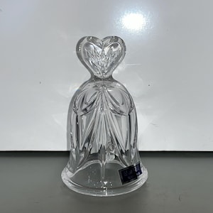 May include: A clear glass bell with a heart-shaped top and intricate crystal designs. The bell has a blue label with the text "Made in China".