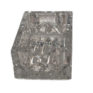 Op de afbeelding: Transparante, geslepen glazen bureau-organizer met een rechthoekige vorm en meerdere compartimenten. Het glas heeft een gedetailleerd, geometrisch patroon. Ontworpen om pennen, potloden of andere kleine kantoorbenodigdheden in op te bergen. Elegant en functioneel ontwerp.