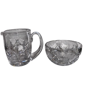 Pode incluir: Um cremeira de cristal transparente com uma pega e uma tigela a condizer. Ambas as peças apresentam um design de vidro cortado com um padrão floral e geométrico. A cremeira tem um bico para facilitar a utilização. O conjunto é ideal para servir natas ou açúcar.