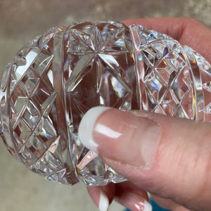 K&ouml;nnte beinhalten: Ein klarer, eif&ouml;rmiger Gegenstand aus geschliffenem Kristall. Der Kristall ist aufwendig mit Diamanten- und Sternmustern geschliffen, die das Licht reflektieren. Das Objekt wird in einer Hand gehalten, was die detaillierte Handwerkskunst und Klarheit des Kristalls zeigt.