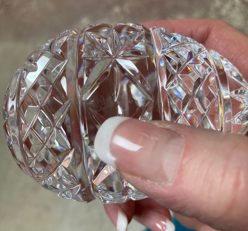K&ouml;nnte beinhalten: Ein klarer, eif&ouml;rmiger Gegenstand aus geschliffenem Kristall. Der Kristall ist aufwendig mit Diamanten- und Sternmustern geschliffen, die das Licht reflektieren. Das Objekt wird in einer Hand gehalten, was die detaillierte Handwerkskunst und Klarheit des Kristalls zeigt.