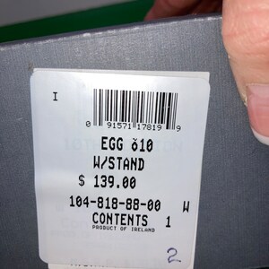 May include: A product label with the text "EGG 010 W/STAND" and a barcode. The label also includes the text "CONTENTS 1" and "PRODUCT OF IRELAND". The label is on a gray surface.