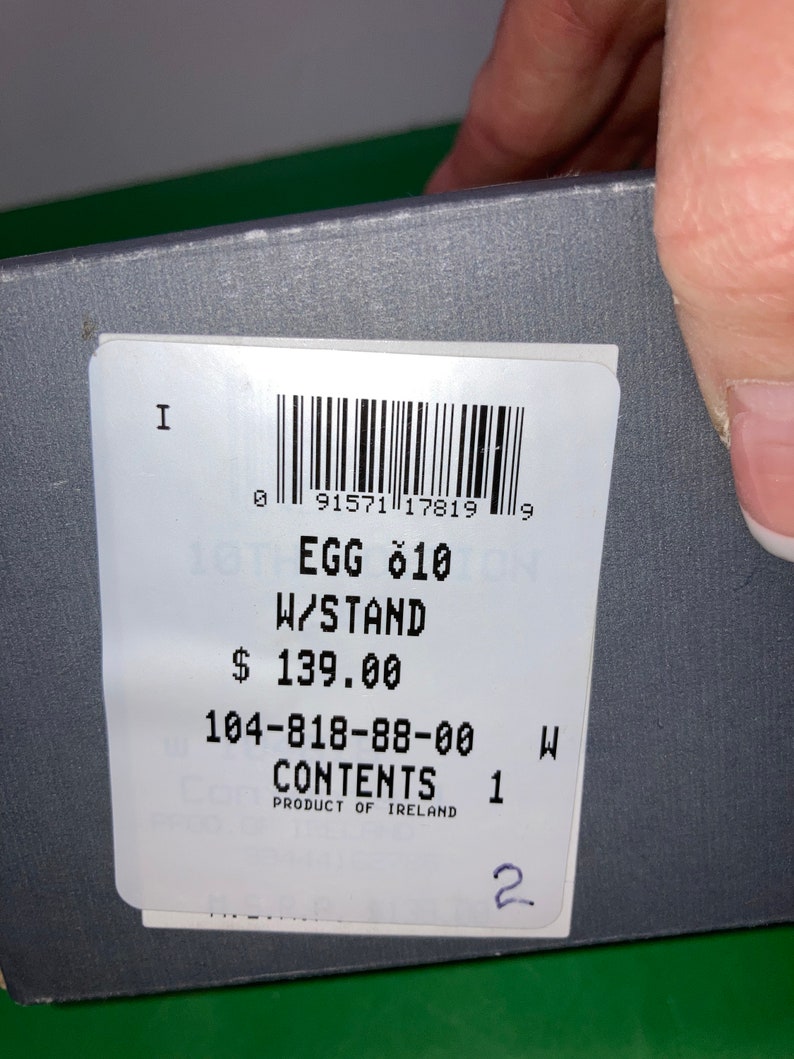 May include: A product label with the text "EGG 010 W/STAND" and a barcode. The label also includes the text "CONTENTS 1" and "PRODUCT OF IRELAND". The label is on a gray surface.