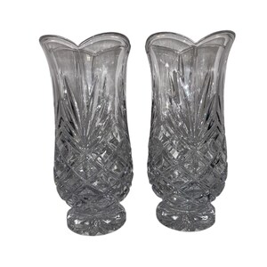 May include: Two clear glass vases with a diamond and leaf pattern. The vases have a scalloped top and a flared shape. The vases are likely for decorative purposes and are made of crystal or a similar material.