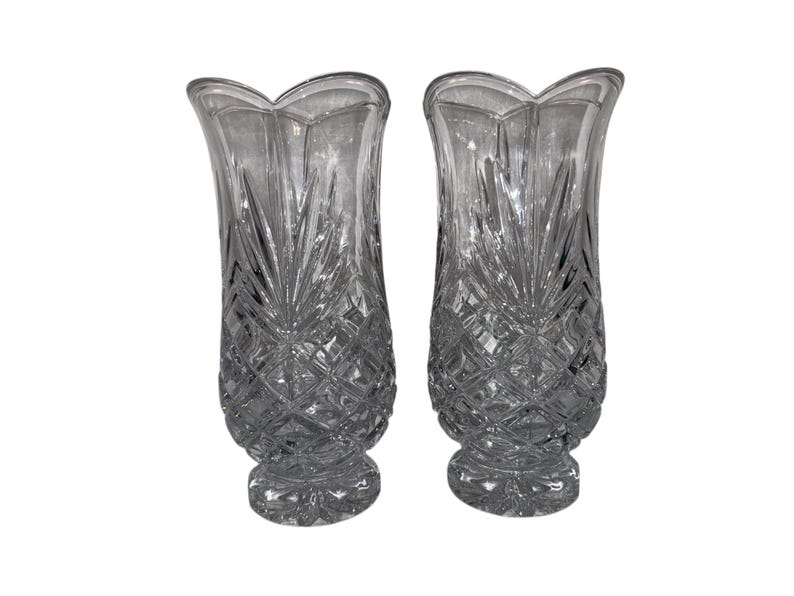 May include: Two clear glass vases with a diamond and leaf pattern. The vases have a scalloped top and a flared shape. The vases are likely for decorative purposes and are made of crystal or a similar material.