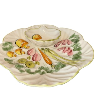 May include: A decorative serving platter with a central dip bowl. The off-white platter features hand-painted illustrations of vegetables and shrimp. The rim and dip bowl are trimmed with a yellow-green color.
