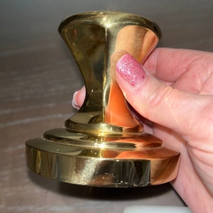 May include: A polished gold metal cabinet knob with a round base and a slightly raised, rounded top.