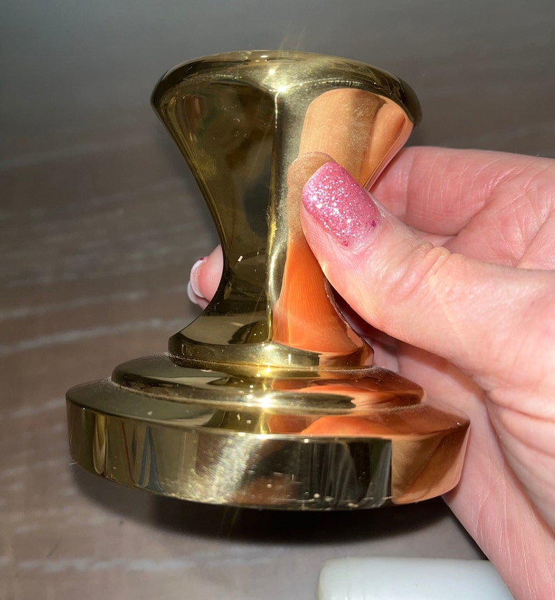 May include: A polished gold metal cabinet knob with a round base and a slightly raised, rounded top.