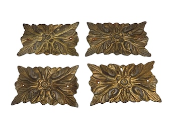 May include: Four antique brass decorative hardware pieces. Each piece is rectangular with a floral and leaf design. The hardware has a distressed, aged appearance with visible wear and tear, and small holes for mounting.
