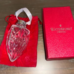 May include: A clear crystal ornament in the shape of a heart with a Waterford Crystal logo on a red velvet bag.