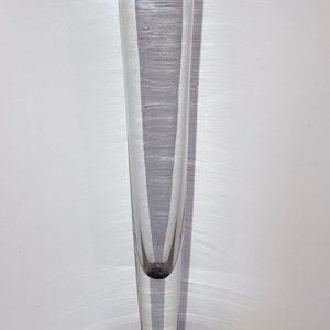 May include: A clear glass bud vase with a black, rounded base. The vase is tall and slender, perfect for displaying a single flower.