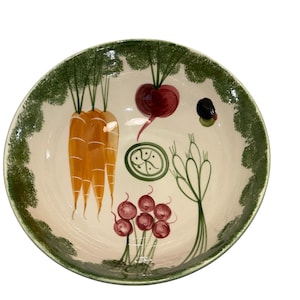 Könnte beinhalten: Eine runde Servierschüssel aus Keramik mit handgemaltem Gemüse-Design. Die Schüssel zeigt Karotten, Radieschen, Rote Bete und anderes Gemüse. Der Rand ist mit einem grünen, blattartigen Rand verziert. Die Schüssel ist cremefarben.