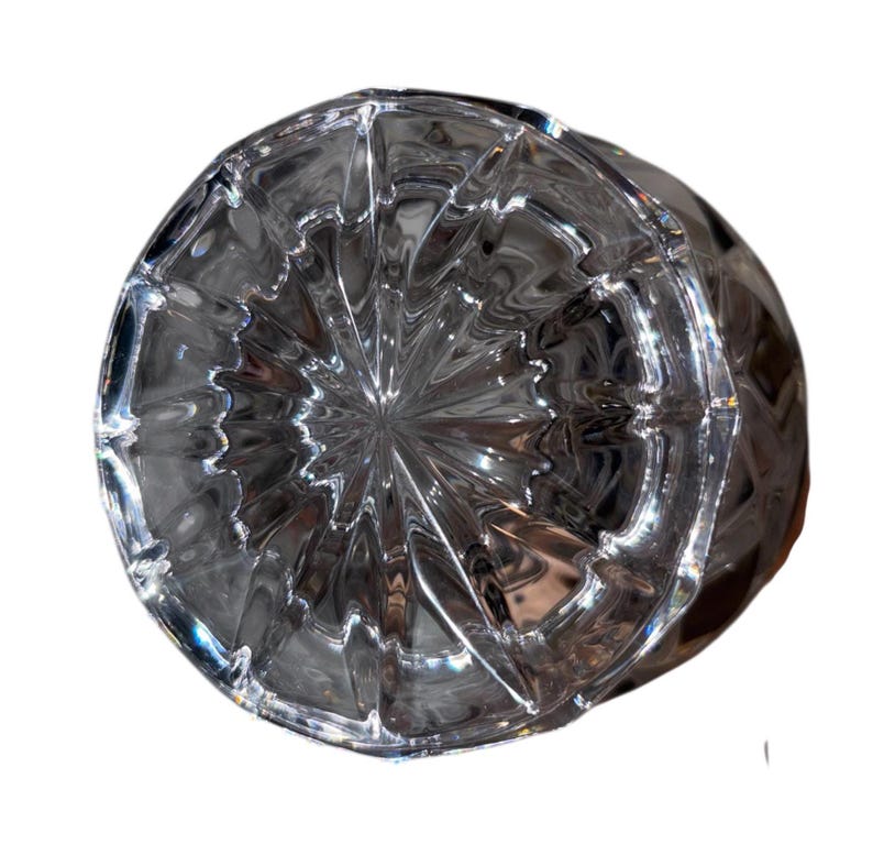 May include: A clear, faceted glass object with a circular base and a textured, geometric pattern. The glass reflects light, creating a sparkling effect. The object appears to be a decorative piece or a part of a larger item.