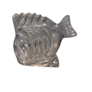 K&ouml;nnte beinhalten: Eine Fischfigur aus klarem Glas mit detaillierten Schuppen und Flossen. Der Fisch hat eine strukturierte Oberfl&auml;che und ist mit einem gebogenen K&ouml;rper und einer markanten Schwanzflosse gestaltet. Die Figur ist ein dekorativer Artikel.
