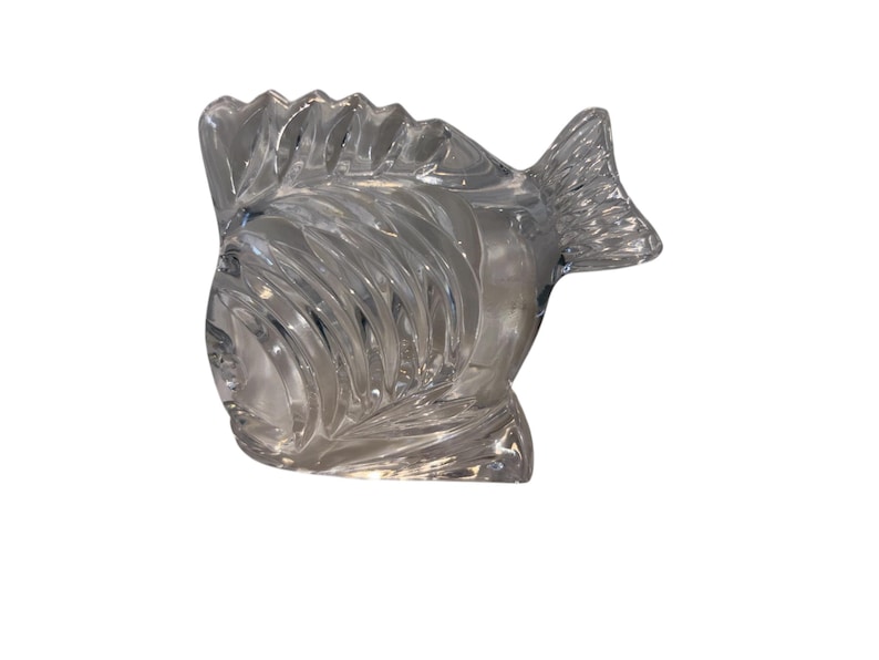 K&ouml;nnte beinhalten: Eine Fischfigur aus klarem Glas mit detaillierten Schuppen und Flossen. Der Fisch hat eine strukturierte Oberfl&auml;che und ist mit einem gebogenen K&ouml;rper und einer markanten Schwanzflosse gestaltet. Die Figur ist ein dekorativer Artikel.