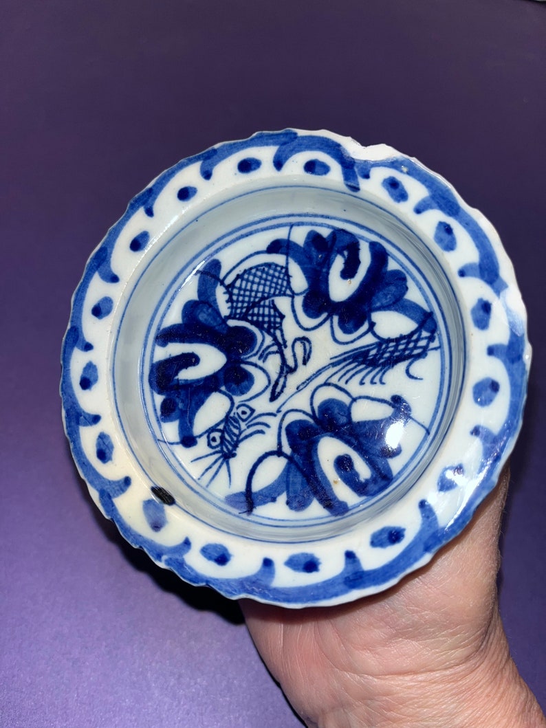 May include: A small, white ceramic dish with a blue and white floral design. The dish has a scalloped edge and a blue rim.