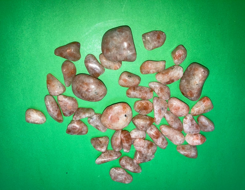 May include: A collection of sunstone tumbled stones in various sizes and shapes. The stones are a light orange color with a shimmery, iridescent finish.