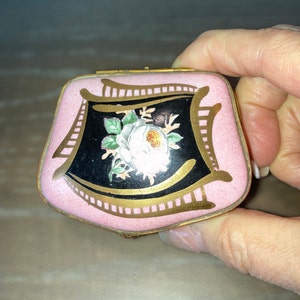 May include: A small pink and black enamel box with a gold trim and a white rose painted on the lid.