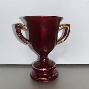 May include: A small, burgundy-colored trophy with gold accents. The trophy has two handles and a round base.