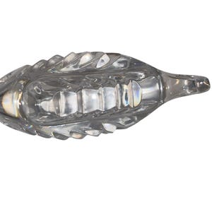 K&ouml;nnte beinhalten: Eine klare Glasschiffchen mit einem strukturierten, blattartigen Design. Das Schiffchen hat einen langen, spitzen Ausguss und einen breiten, oval geformten K&ouml;rper. Das Glas ist transparent und l&auml;sst Licht durch.