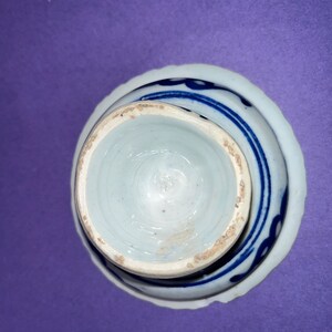 May include: A white porcelain bowl with a blue and white design. The bowl is turned upside down, showing the bottom of the bowl.
