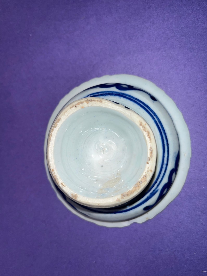 May include: A white porcelain bowl with a blue and white design. The bowl is turned upside down, showing the bottom of the bowl.