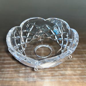 May include: A clear glass crystal chandelier prism with a scalloped edge and a cut-out design. The prism has a small hole in the center.