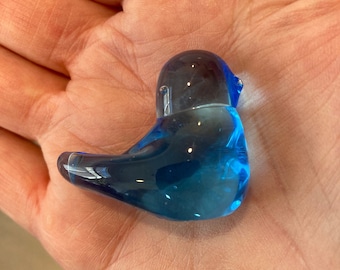 Peut inclure: Petite figurine d'oiseau en verre bleu transparent. L'oiseau est assis, la tête levée et le bec légèrement ouvert. Le verre est d'un bleu profond et vibrant, avec une finition lisse et brillante. La figurine mesure environ 7,6 cm de long.