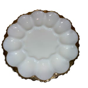 May include: A white, scalloped-edge serving dish with a gold-colored rim. The dish has a central circular area surrounded by 12 rounded compartments. The dish is likely made of glass or ceramic.