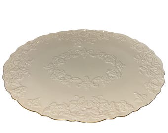 Könnte beinhalten: Eine cremefarbene, ovale Servierplatte mit gewelltem Rand und goldenem Rand. Die Platte hat ein erhabenes, verziertes Blumen- und Blattdesign um den Rand und die Mitte. Ein dekoratives Stück zum Servieren von Speisen.