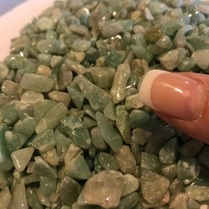 May include: A close-up image of a pile of small, light green, translucent stones. The stones are smooth and have a natural, irregular shape.