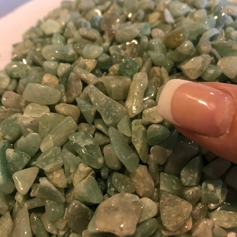 May include: A close-up image of a pile of small, light green, translucent stones. The stones are smooth and have a natural, irregular shape.