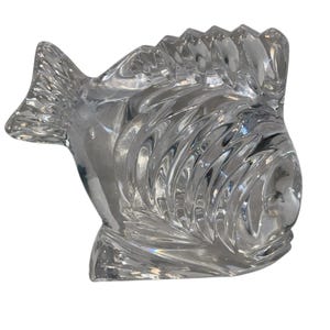 K&ouml;nnte beinhalten: Eine klare Glasfischfigur mit detaillierten Schuppen und Flossen. Der Fisch hat eine strukturierte Oberfl&auml;che und ein stilisiertes Design. Diese dekorative Figur eignet sich zur Pr&auml;sentation.
