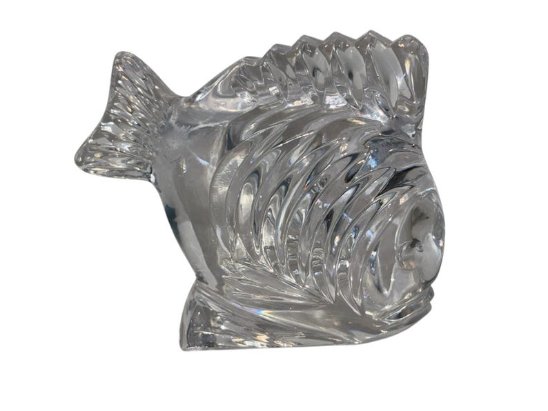 K&ouml;nnte beinhalten: Eine klare Glasfischfigur mit detaillierten Schuppen und Flossen. Der Fisch hat eine strukturierte Oberfl&auml;che und ein stilisiertes Design. Diese dekorative Figur eignet sich zur Pr&auml;sentation.