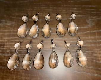 May include: Ten crystal teardrop-shaped chandelier prisms with silver metal tops. The prisms are clear and have a faceted design.