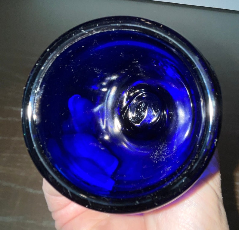 Peut inclure: Un bouchon de bouteille en verre bleu cobalt avec un dessus lisse et arrondi. Le bouchon pr&eacute;sente une l&eacute;g&egrave;re indentation au centre.