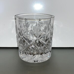 Könnte beinhalten: Ein klarer Glasbecher mit geschliffenem Glasdesign. Das Glas hat ein Diamantenmuster mit einem floralen Motiv.