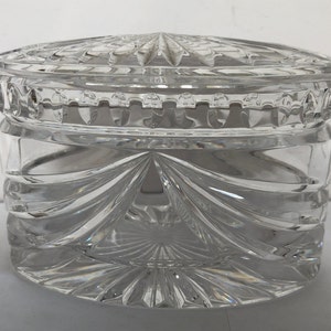 May include: A clear glass jar with a lid, both featuring intricate cut-glass designs. The jar is round and has a wide opening.