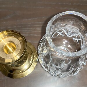 May include: A gold metal candle holder with a round base and a clear glass votive holder with a cut glass design.