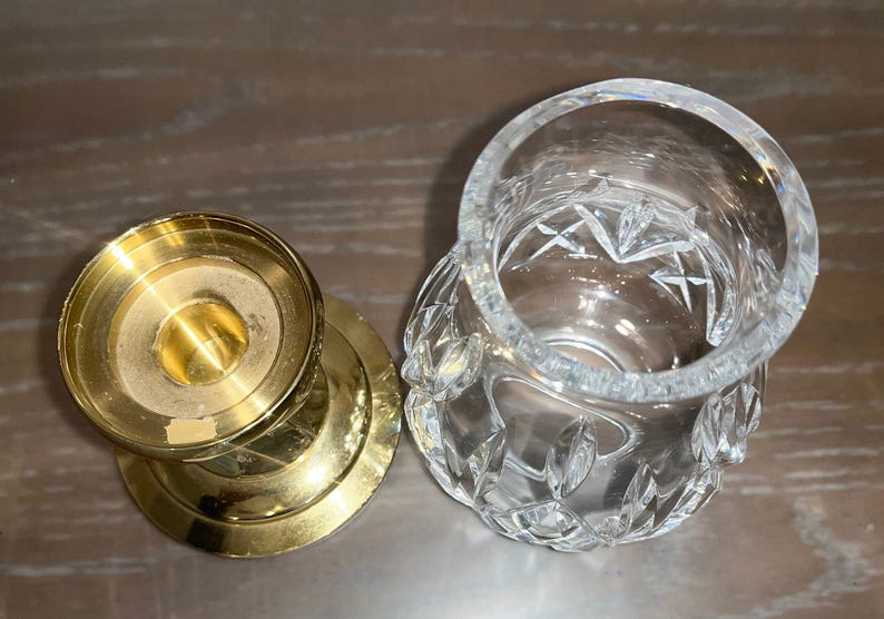 May include: A gold metal candle holder with a round base and a clear glass votive holder with a cut glass design.