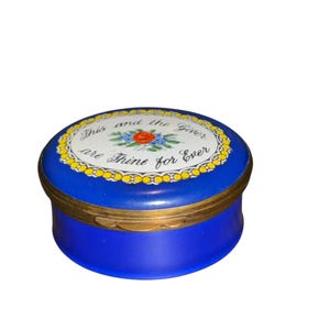Peut inclure: Une boîte à bijoux ronde bleu cobalt avec un bord doré. Le couvercle présente un centre blanc avec un motif floral et les mots "This and the Giver are Thine for Ever".