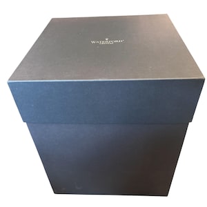 May include: A dark grey, rectangular box with a lid, possibly for a gift. The box features the "WATERFORD CRYSTAL" logo on the top. The box is set against a white background.