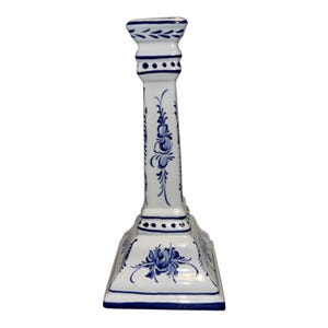Puede incluir: Un candelabro de cerámica blanca con motivos florales y patrones geométricos pintados a mano en azul. El diseño de columna con base cuadrada presenta un borde superior ensanchado y líneas azules detallando los lados y la base.