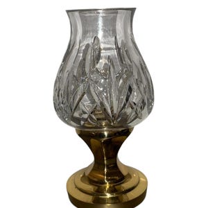 May include: A clear crystal candle holder with a cut glass design sits on a gold metal base.