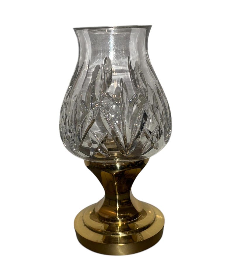 May include: A clear crystal candle holder with a cut glass design sits on a gold metal base.