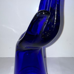 Peut inclure: Une sculpture de main en verre bleu cobalt. La main est ouverte et les doigts sont tendus. La sculpture est faite de verre &eacute;pais et a une finition lisse et polie.