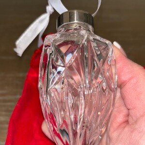May include: A clear glass Christmas ornament with a faceted design. The ornament has a silver metal cap and a white ribbon.