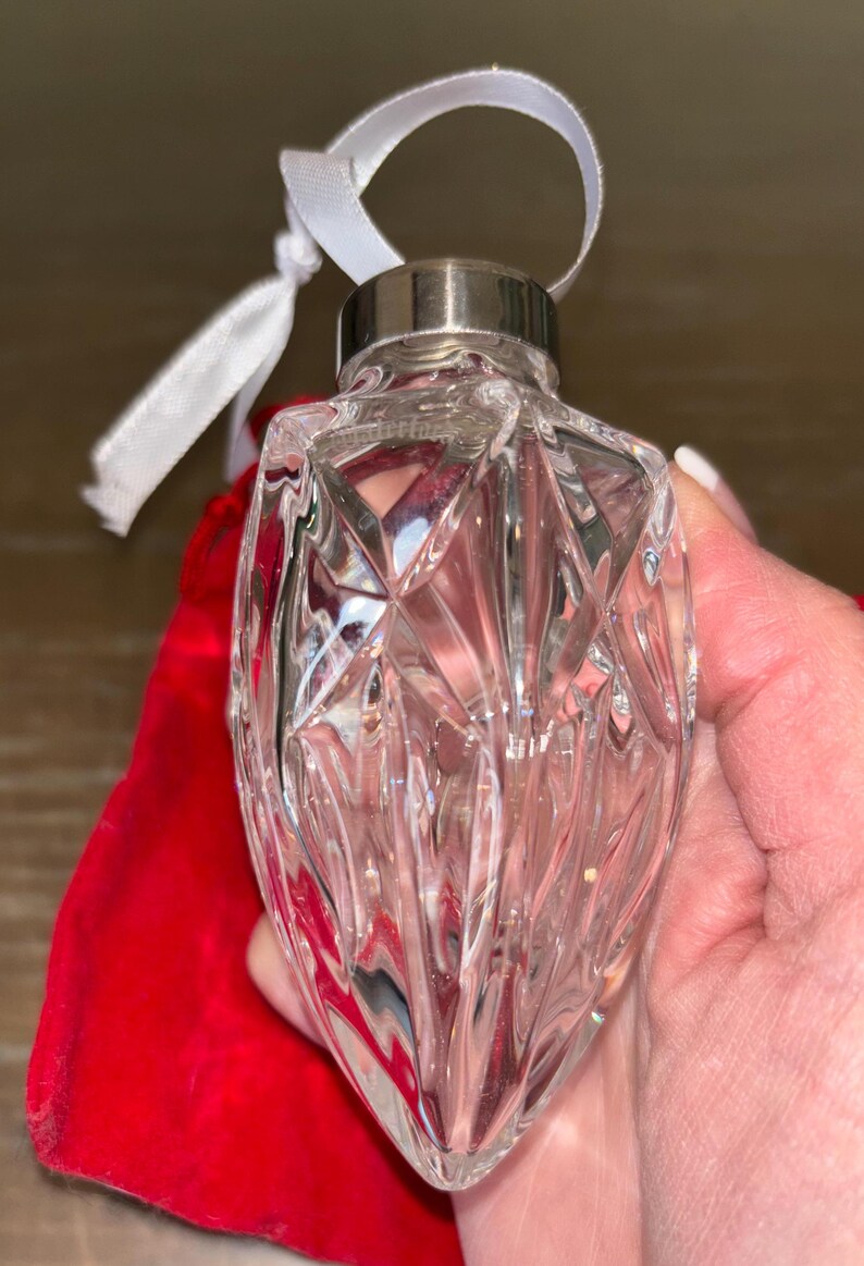 May include: A clear glass Christmas ornament with a faceted design. The ornament has a silver metal cap and a white ribbon.