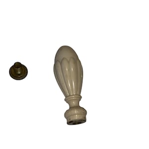May include: Ivory-colored finial with a decorative, fluted design. The finial has a bulbous shape and a brass-colored screw. This decorative element is likely for furniture or home decor.